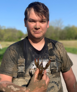 Swedberg, muddy and holding a crayfish.